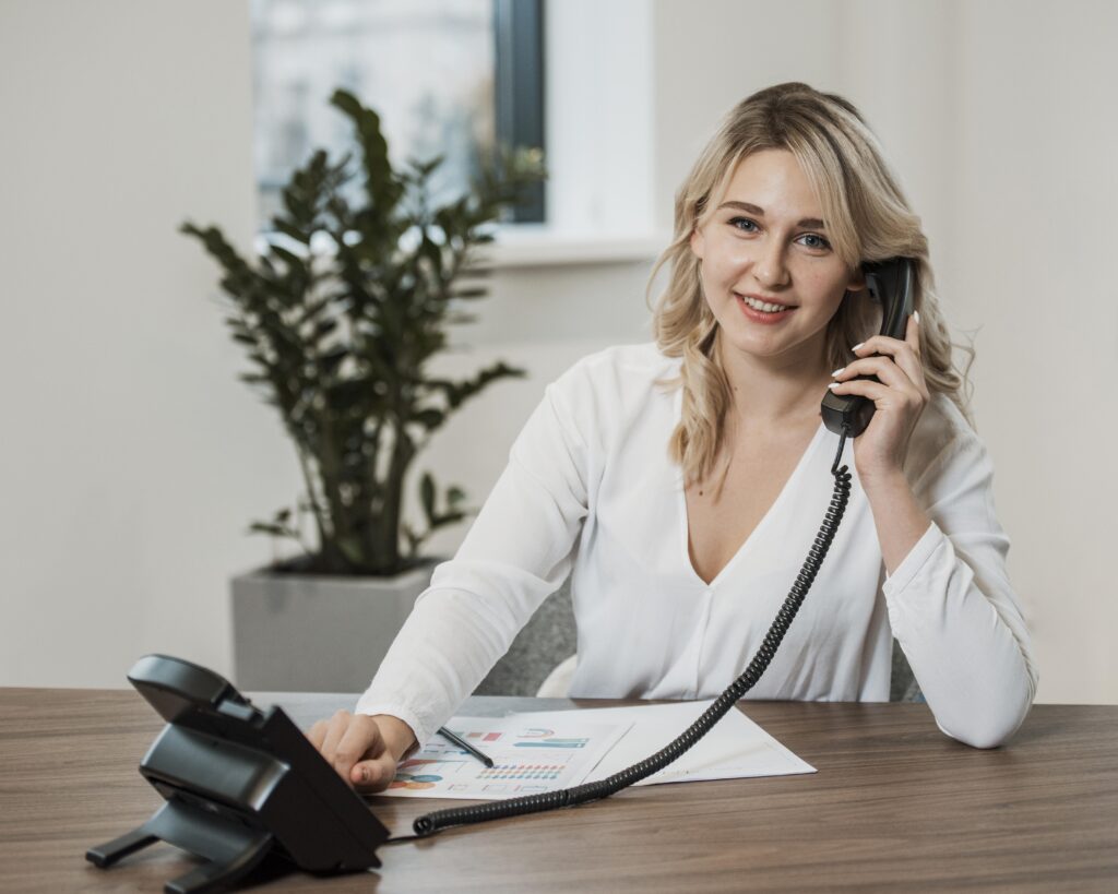 Smiling woman talking on a phone at a desk.