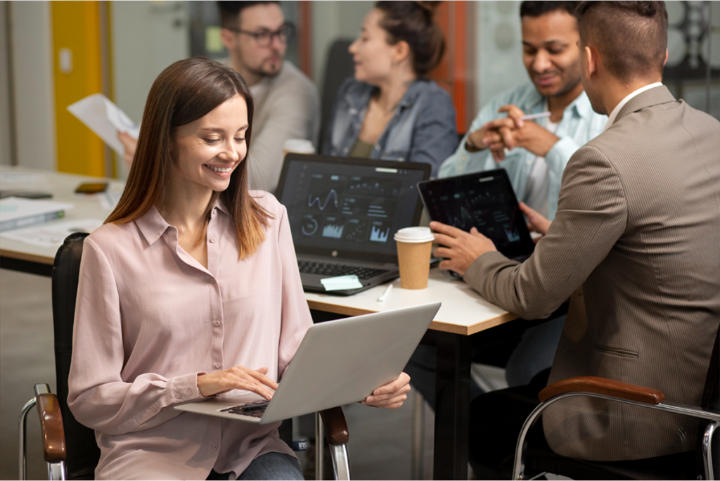 A group of professionals collaborating in a modern office, with a woman working on her laptop.